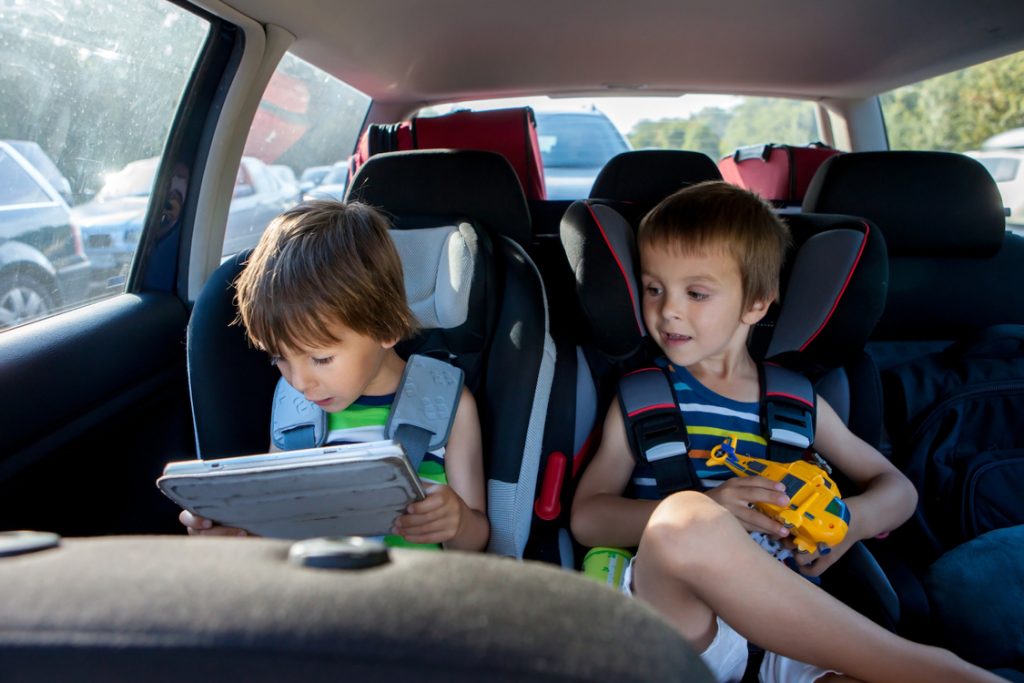Two boy in children car seats traveling by car and playing with toys and tablet summertime