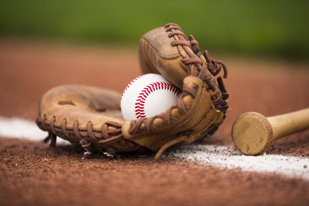 baseball inside of a glove, on the ground , next to a bat. 
