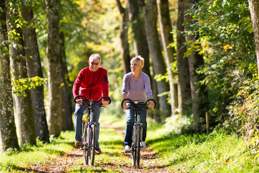 Older man and woman biking through a bicycle path near trees and leaves 
