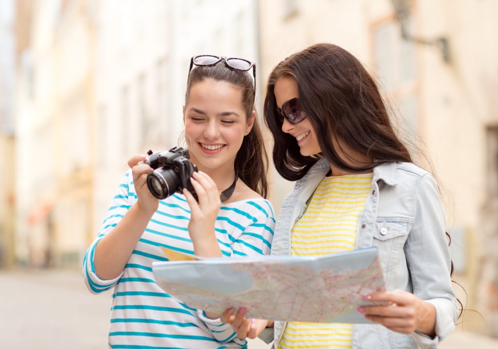 Two young attractive women are touring a new city, with a camera and map in their hands