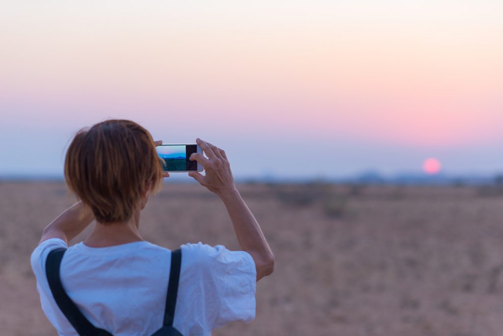 Woman tourist with her smart phone, photographing the romantic desert sunset