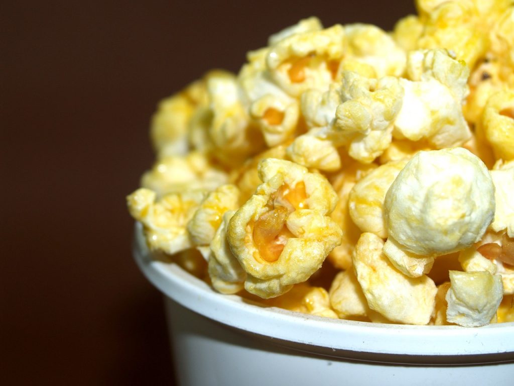 buttery popcorn upclose in a white bucket, with a brown background 