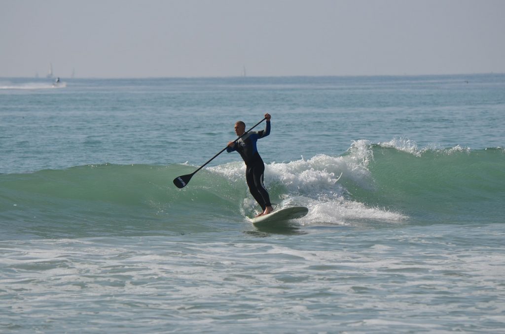 man wearing a wetsuit paddle surfing in the ocean 