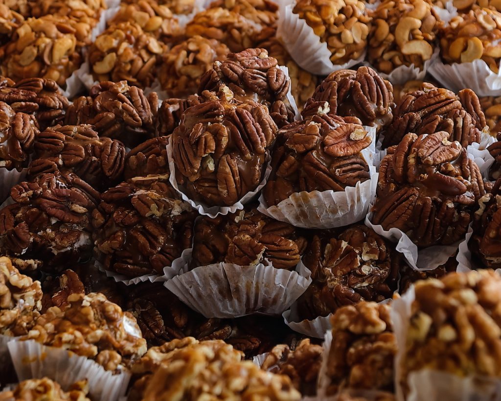 Picture of many tasty individually wrapped chewy pecan praline bites, ready to eat. showing, shallow depth of field with walnuts in front and behind them.